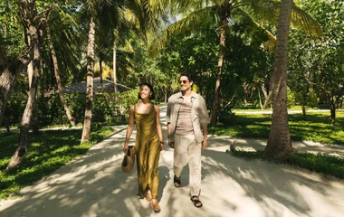 Casal andando de mãos dadas em uma área arborizada no resort.