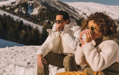 Casal bebendo chocolate quente em uma xícara olhando paisagem de neve.