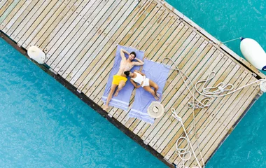 casal deitado em deque de madeira sobre águas azuis