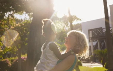 mãe com filha no colo sorrindo contra o sol