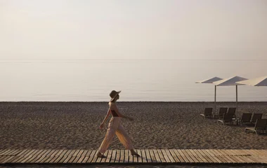 mulher caminhando em deque de madeira sobre areia da praia