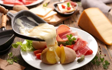 Raclette sendo colocado num prato com batata e outros aperitivos.