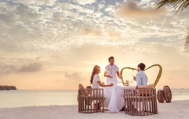 Couple enjoying dinner on the beach being assisted by butler