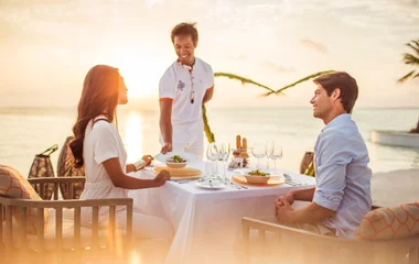 Couple enjoying dinner on the beach being assisted by butler