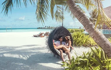 Couple cuddling in a hanging chair on the beach under palm trees