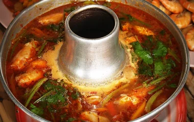 Zuppa Tom Yam Kung thailandese con gamberi, funghi e peperoncino servita in piatto tradizionale con candela per mantenerla calda