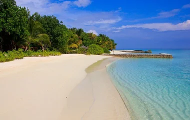 Spiaggia bianca con mare cristallino e palafitte in lontananza alle Maldive