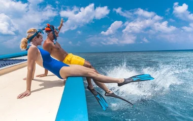 Una coppia in costume con boccaglio e pinne al bordo di una barca pronti allo snorkeling