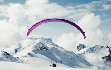 Pessoa praticando parapente com vista para os Alpes nevados.