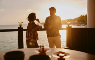 Casal em pé tomando drink ao por do sol