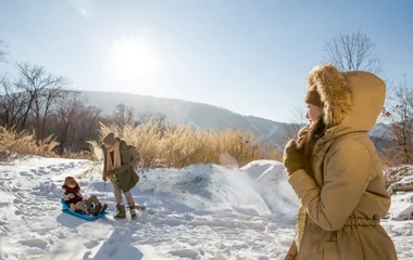 Uma família em uma montanha coberta de neve enquanto o pai puxa seu filho em uma prancha de plástico pela neve