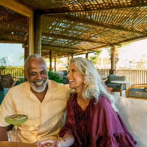 Um casal de homem e mulher 60+ sorrindo tomando um drink no bar
