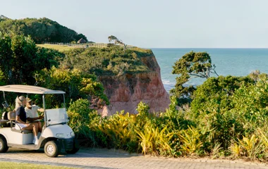 Casal dentro de um carrinho de golfe com vista de falésia e mar perto ao Club Med Trancoso.
