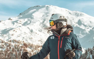 une femme face à une montagne avec un casque et un masque de ski